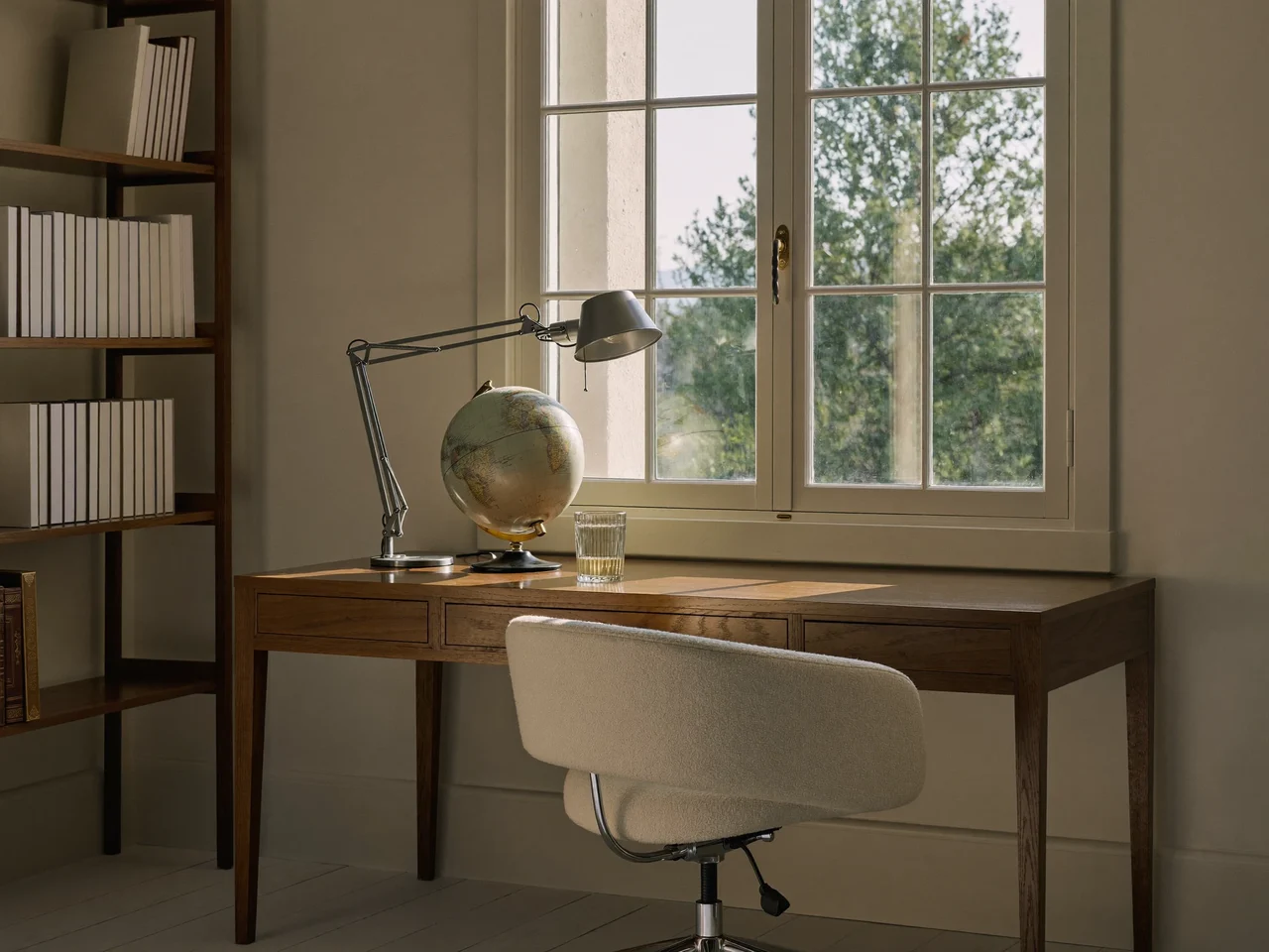 Stille studiehjørne ved vindue med lampe, bogreol og tom stol
